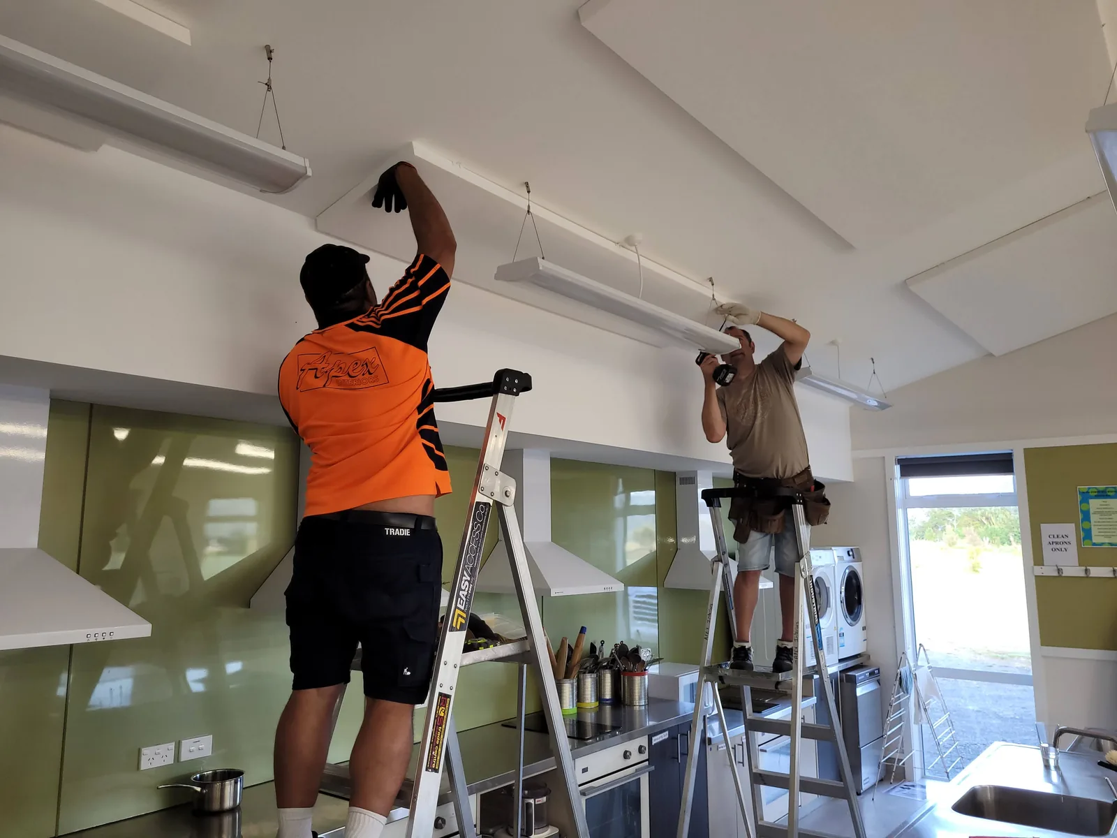 Contractors fitting acoustic panels around classroom lighting